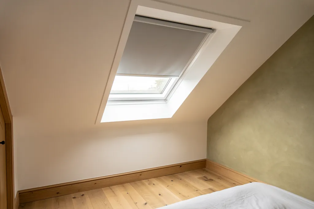 A roof window with a blackout blind half drawn